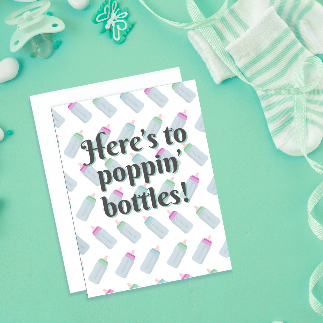 A photo of a baby card. It has baby bottles as a pattern in the back. Text reads, Here's to Poppin' Bottles!